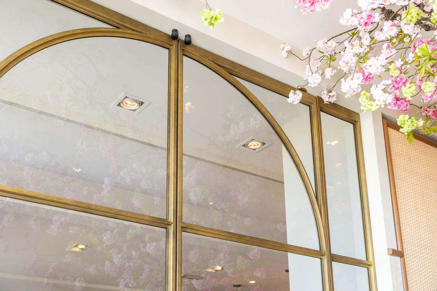Messing stalen schuifdeur met glas en sierlijke boogdetails, elegant gecombineerd met bloesemdecoratie in een luxe interieur.